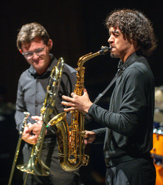 A trombone player looks on as a saxophone player solos